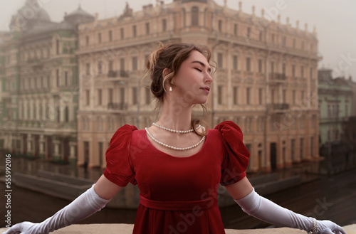 Принти на полотні Beautiful young girl in a nineteenth century dress stands on a balcony in front of a beautiful building