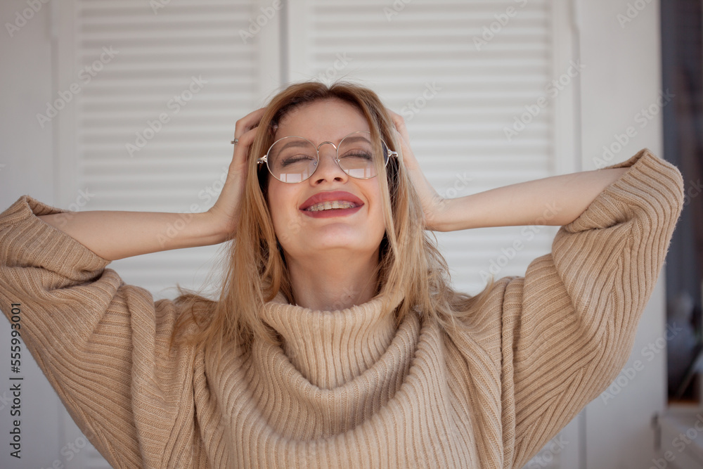 Stylish and beautiful young student with glasses and beige oversize sweater. Young woman wearing braces and smiling Stylish and beautiful young student with glasses and beige oversize sweater. Young woman wearing braces and smiling