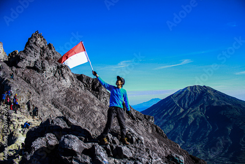 A Young Asian Male Hiker Is on a Mountain Top with a Waving Flag