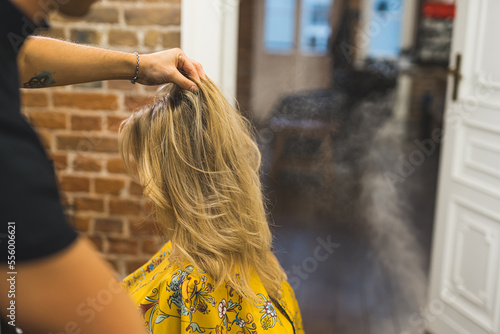 New haircut in a professional salon. Unrecognizable hairstylist touching the blond hair of his client. Blurred background. Copy space. High quality photo