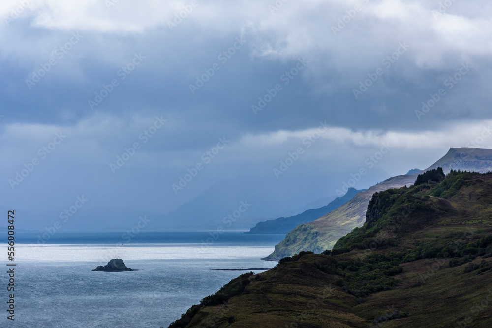 Sunlit ocean with sea cliffs and rain clouds along the coast of the Isle of Skye in Scotland, United Kingdom