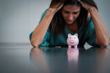 negative thinking woman with dark hairs looking depressed to her pink piggy bank while being scary & worried about future and her savings with elbows on the floor and hands over head