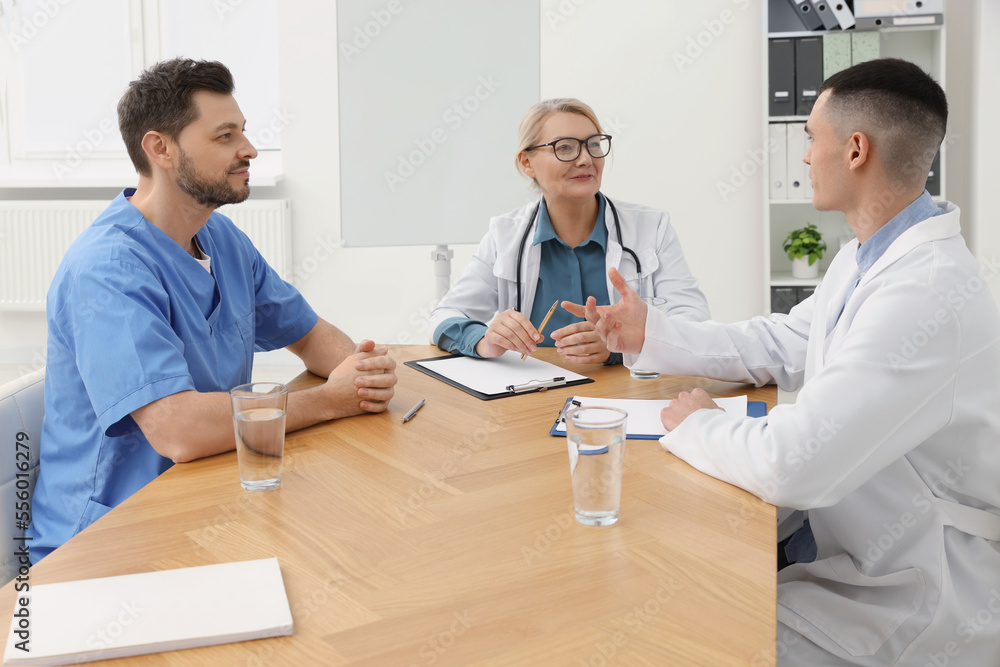 Obraz premium Medical conference. Team of doctors having discussion at wooden table in clinic