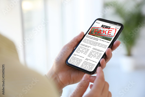 Fake information. Woman using mobile phone to read news at home, closeup