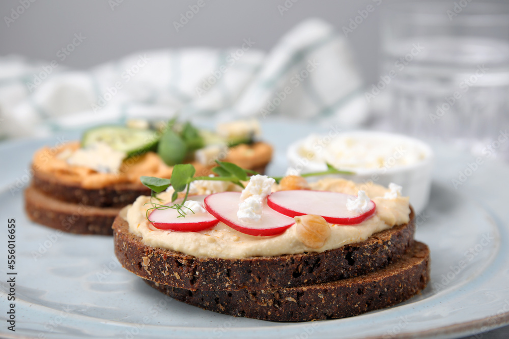 Delicious sandwiches with hummus and different ingredients on plate, closeup
