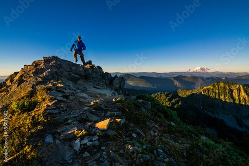 Athletic adventurous male hiker, hiking down a ridge on top of a mountain with Mount Rainier in the background during a beautiful sunrise. 
