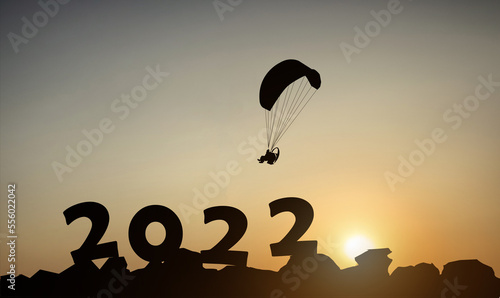 Silhouette of a paramotor with the numbers 2022 on the mountain at sunset against the background of the morning sunlight.