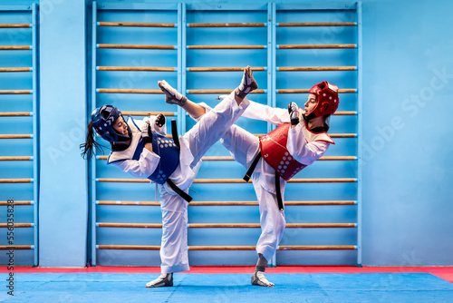 Portrait of two young women in kimono and suture, taekwondo athletes wrestling in the gym. Sportswomen demonstrating taekwondo martial art, hard training concept photo