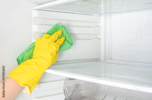 Hand cleaning refrigerator. Person washing refrigerator with rag. Housekeeper wipes shelves of clean refrigerator. Hand in yellow rubber protective glove and green sponge washes. copy space