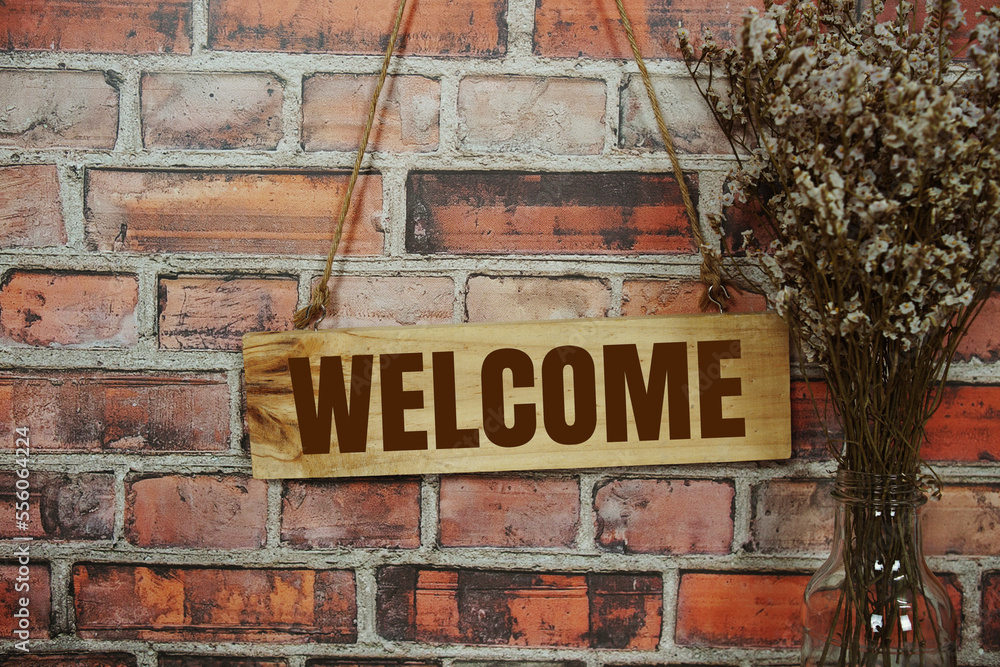 Welcome sign text message on wooden board hanging on old brick wall background