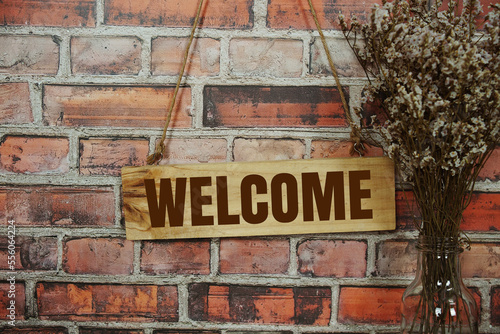 Welcome sign text message on wooden board hanging on old brick wall background