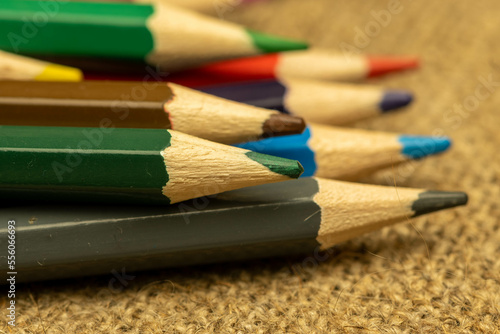 Several colored pencils of different colors on a background of coarse burlap. Close-up, selective focus.