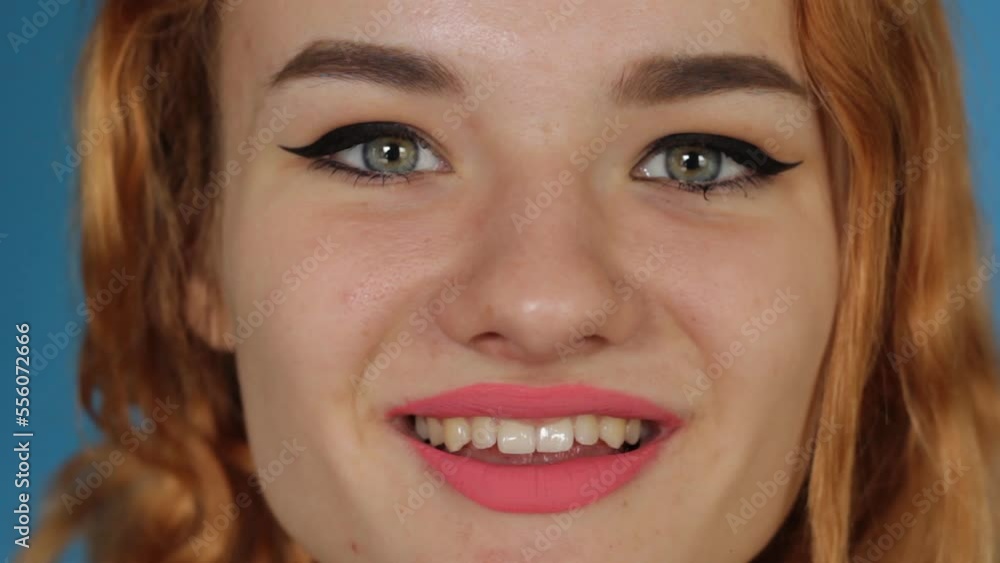 Close-up macro of a young beautiful woman smiling while looking at the camera. Red hair blue background. Close-up macro of a young beautiful woman smiling while looking at the camera. Red hair blue background.