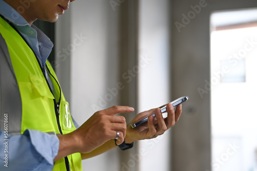 Cropped shot of engineer man wearing reflective jackets standing in construction site and using smart phone