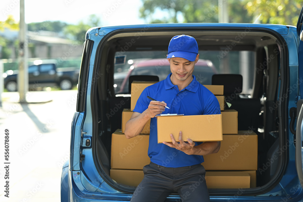 Image of delivery man sitting in open delivery van and checking checking address details of client on clipboard Image of delivery man sitting in open delivery van and checking checking address details of client on clipboard
