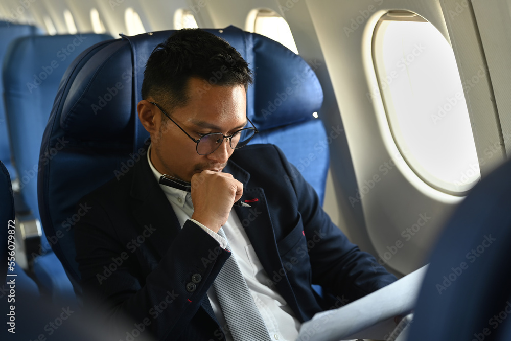 Focused businessman working with financial document while sitting on airplane cabin. Business or travel abroad concept
