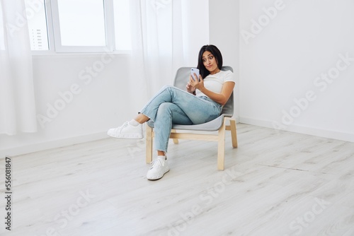 Woman sitting on chair with phone in hand in new apartment, online shopping via phone, online shopping