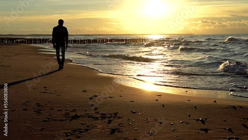 Man walking on a beach at golden sunset. Wavy Baltic sea with breakwater. Normal speed.