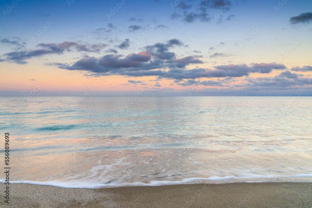 calm turquoise ocean water under a olorful sunset sky with calm waves on the sandy shore