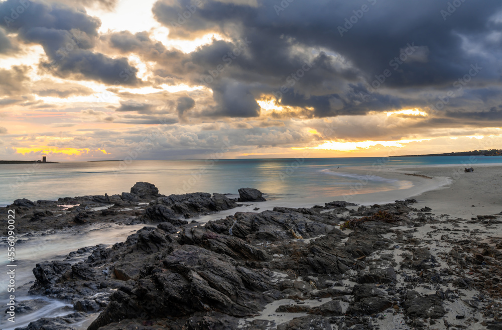 view of La Pelosa beach in Sardinia at sunrise with rocky reef in the foreground