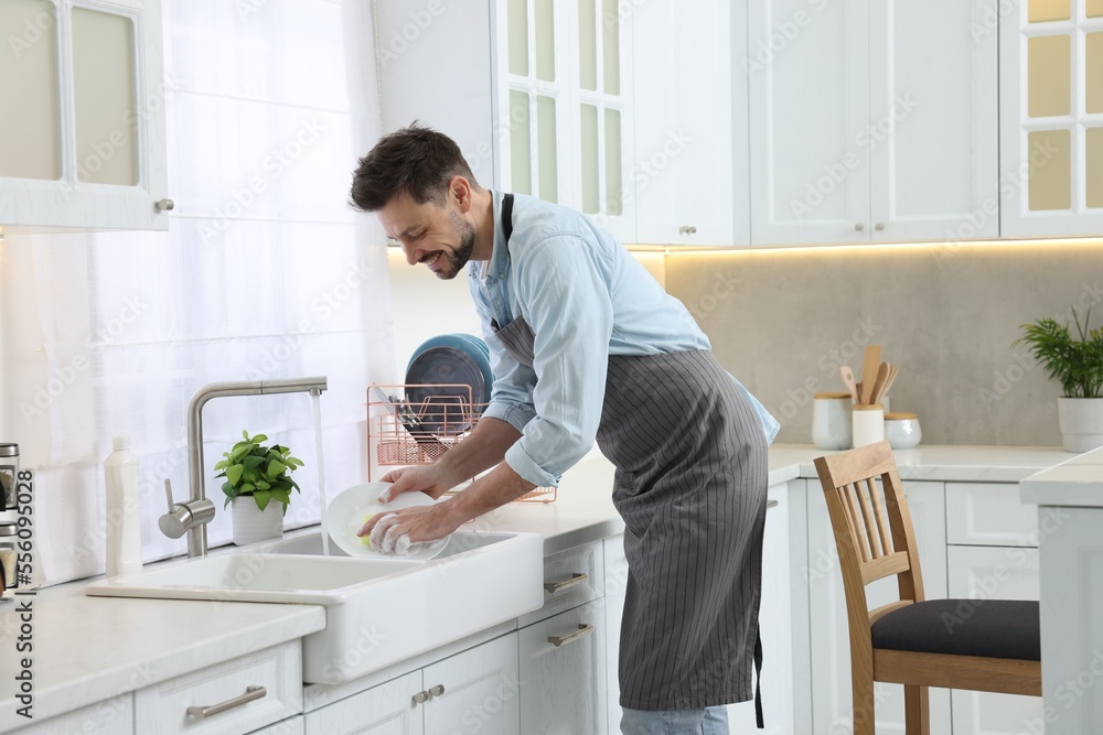 Man washing plate above sink in kitchen