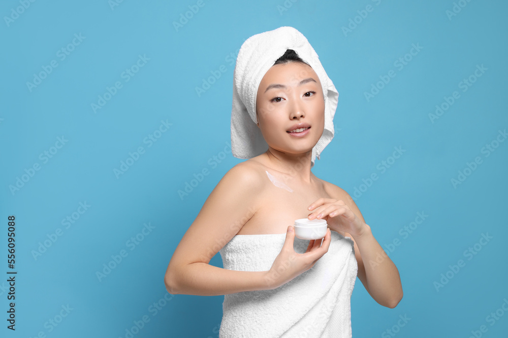 Beautiful young Asian woman with jar of body cream on light blue background, space for text Beautiful young Asian woman with jar of body cream on light blue background, space for text