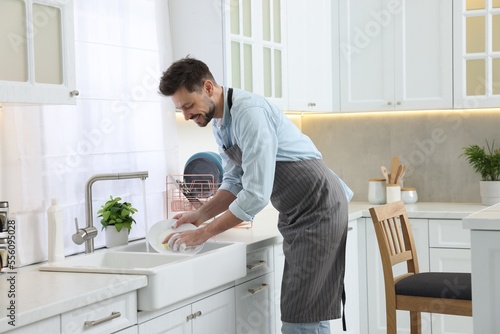 Man washing plate above sink in kitchen