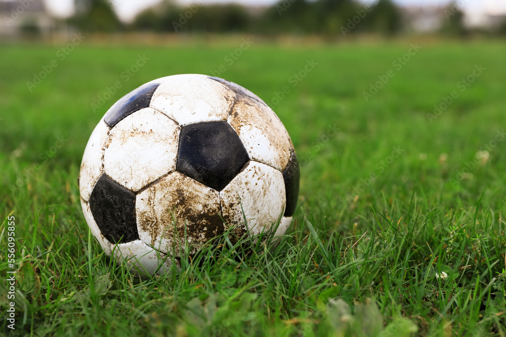 Dirty soccer ball on green grass outdoors, space for text