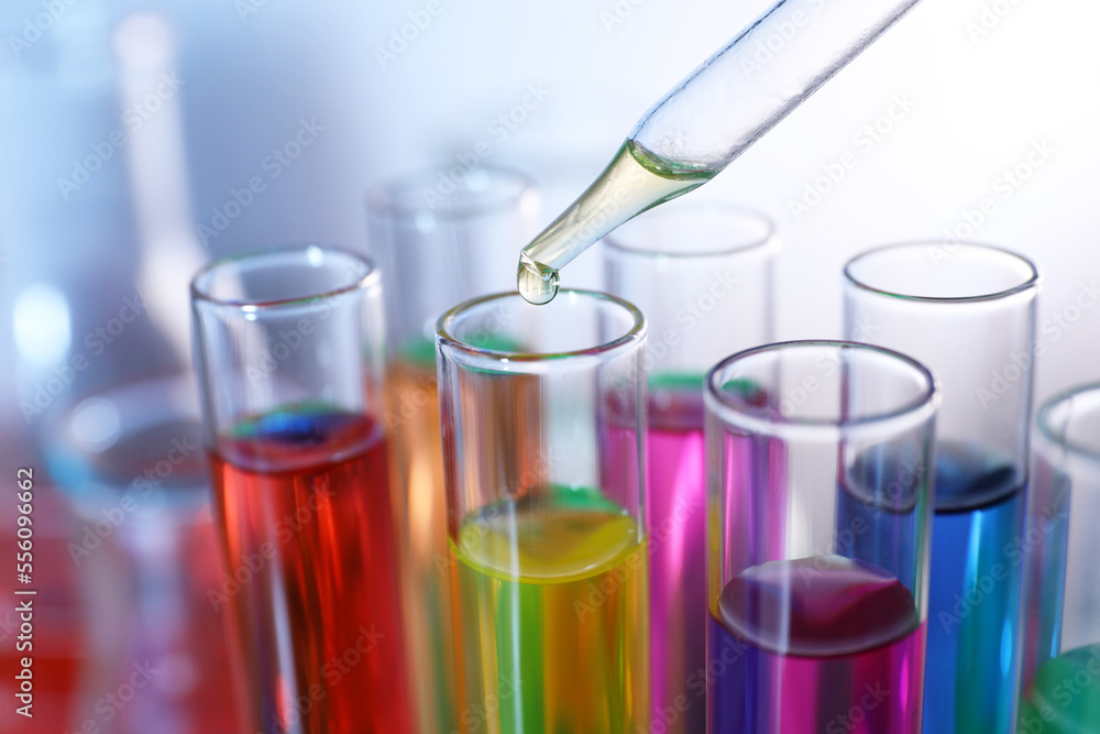 Dripping liquid from pipette into test tube on blurred background, closeup Dripping liquid from pipette into test tube on blurred background, closeup