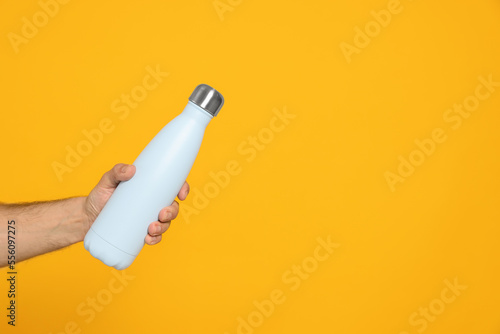 Man holding thermo bottle on orange background, closeup. Space for text