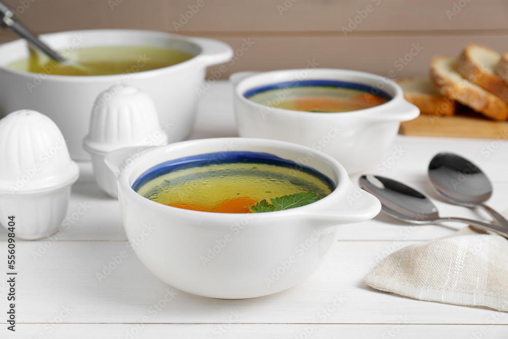 Delicious chicken bouillon with carrot and parsley on white wooden table, closeup Delicious chicken bouillon with carrot and parsley on white wooden table, closeup