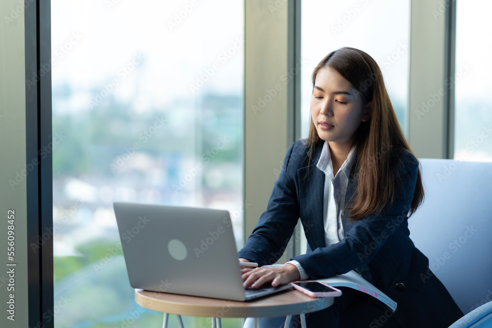 Businesswoman sitting and reading a book by the window of the office. Used in marketing business media, insurance, life insurance, finance Businesswoman sitting and reading a book by the window of the office. Used in marketing business media, insurance, life insurance, finance