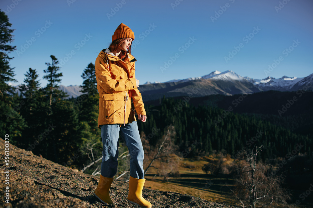 Woman full-length hiker standing frozen on the mountain looking at nature happiness with a view of the mountains in a yellow raincoat travel and hiking in the mountains at sunset freedom