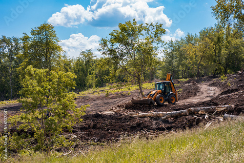 a tractor with a bucket rows branches and cleans the park