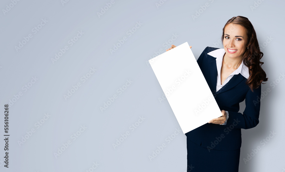 Happy smiling woman in black confident suit showing blank white signboard. Business and advertising concept. Copy space empty place for text. Gray color background.. Happy smiling woman in black confident suit showing blank white signboard. Business and advertising concept. Copy space empty place for text. Gray color background..
