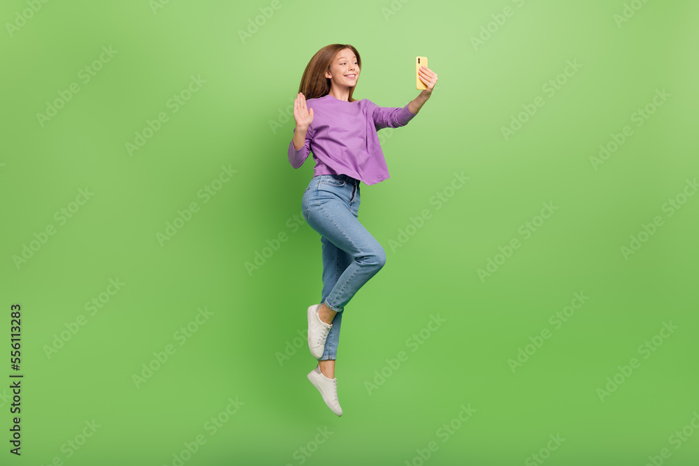 Full length photo of optimistic positive girl straight hairdo purple pullover waving hand hold phone isolated on green color background Full length photo of optimistic positive girl straight hairdo purple pullover waving hand hold phone isolated on green color background