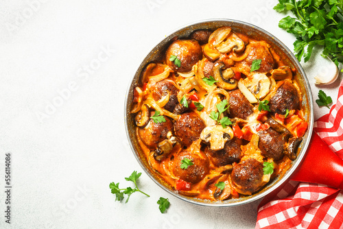 Meatballs with mushrooms in tomato sauce in a frying pan.