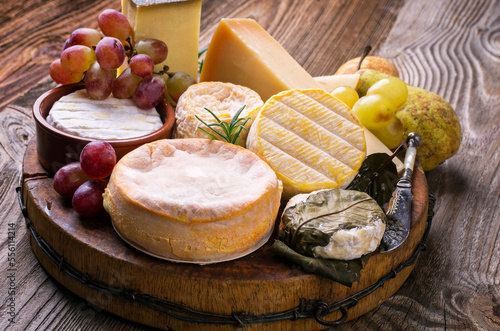 Traditional French cheese platter with soft and hard cheese and fruits served as close-up on a rustic wooden board photo