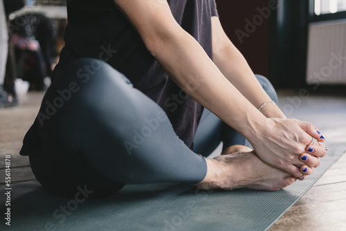Close-up photo of the legs and torso of a female yogi meditating barefoot and wearing leggings in cobbler's pose on a yoga mat on the floor
