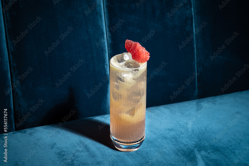 Cocktail on blue background. Modern, stylish drink placed on velvet couch at the bar, night club or restaurant. Refreshing alcoholic beverage with grapefruit and gin in highball glass. Copy space