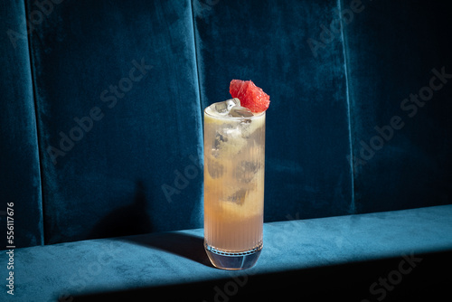 Cocktail on blue background. Modern, stylish drink placed on velvet couch at the bar, night club or restaurant. Refreshing alcoholic beverage with grapefruit and gin in highball glass. Copy space