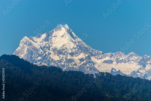 Kangchenjunga, also spelled Kanchenjunga, Kanchanjangha, and Khangchendzonga is the third-highest mountain in the world. The snow-clad peak of the mountain towers above the thick green forest. photo