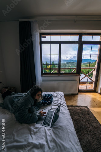 Young woman working on laptop while lying on bed © teksomolika