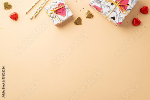 Valentine's Day concept. Top view photo of present boxes heart shaped chocolate candies straws and golden confetti on isolated pastel beige background with copyspace