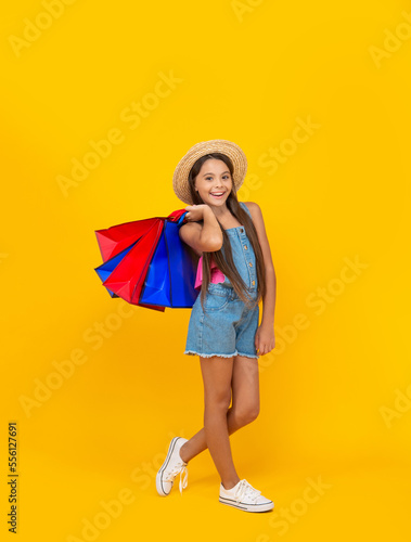 cheerful teen kid with shopping bags on yellow background. full length