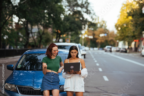 Two young women with a laptop near the car