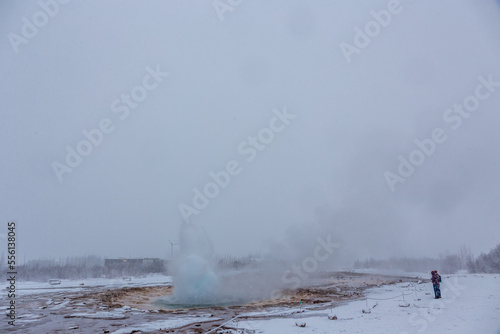 Geyser in fase iniziale di eruzione mentre si sta creando la bolla azzurra durante una nevicata e due persone che guardano