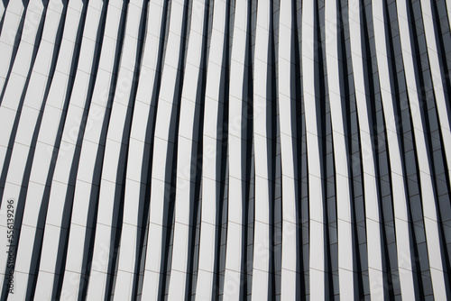 Fragment of facade of tall modern blue building with contrast shadows and long winding lines. Abstract architecture photo background. Business quarter in a modern city. Urban scene pattern, texture.