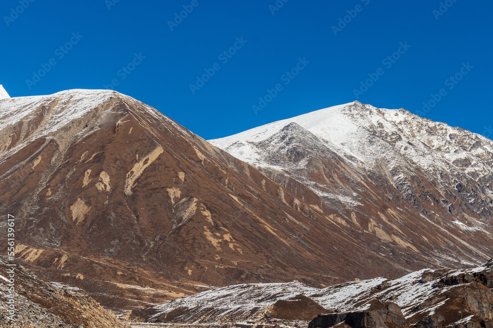 Snow-capped rocky brown mountains of mighty Himalayas amid the clear blue sky.