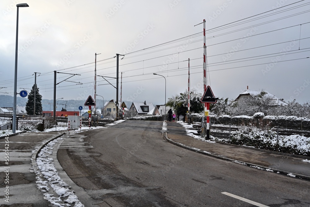 Railway crossing in village Urdorf, Switzerland in winter, captured  with open barriers. Photo shows the road in direction to village, some houses are on the background. Copy space is on foreground.